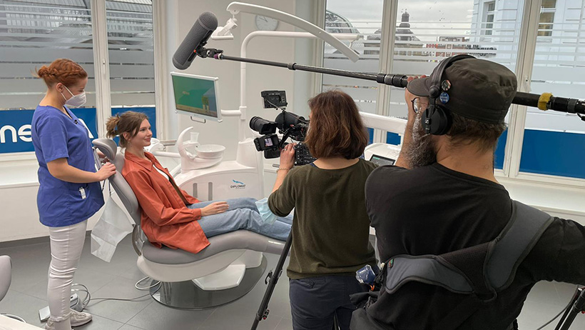 Filmteam dreht in einer Zahnarztpraxis, während eine Patientin im Behandlungsstuhl sitzt und von einer zahnmedizinischen Fachangestellten betreut wird