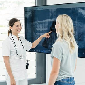 Ärztin und Patientin schauen Röntgenbild auf einem großen Bildschirm an